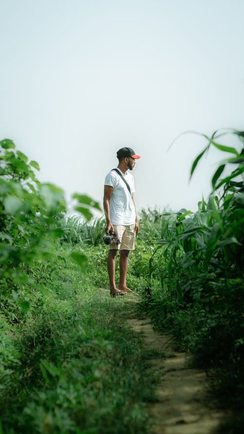 Free Man standing on a footpath surrounded by greenery in a serene outdoor setting. Stock Photo