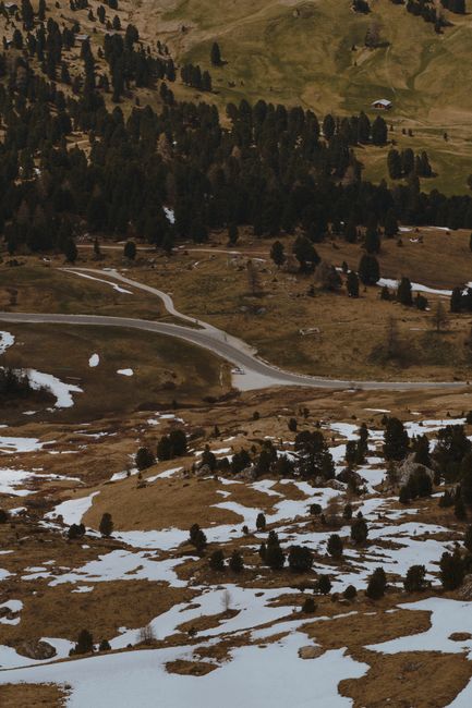 Aerial view of a snowy mountain landscape with a winding road through trees and grass.
