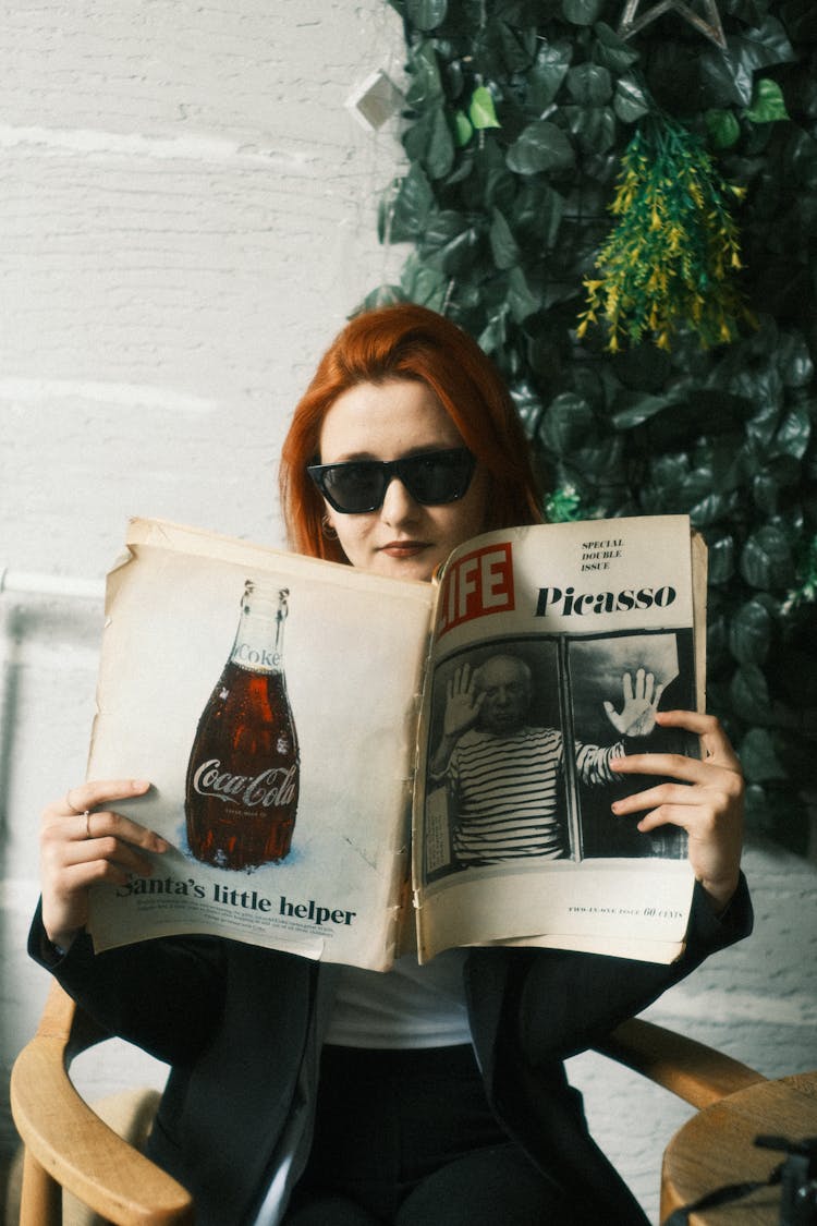 Woman In Sunglasses Sitting And Reading A Vintage Newspaper