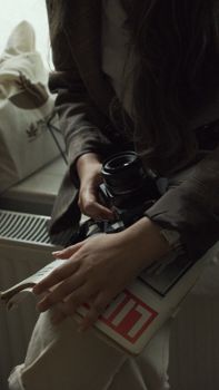 A woman sits indoors holding a camera and a magazine, creating a relaxed, vintage atmosphere.