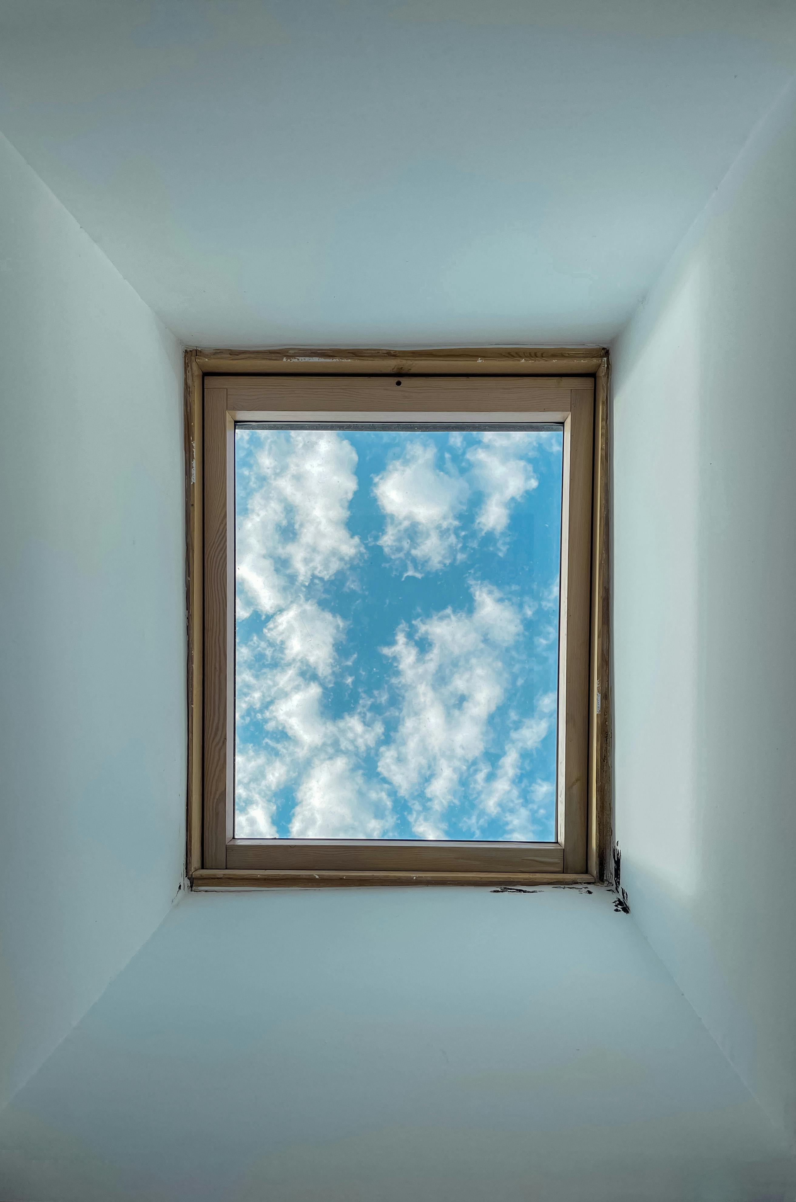 A skylight window showing a clear blue sky with fluffy clouds, photographed indoors in Lisbon, Portugal.
