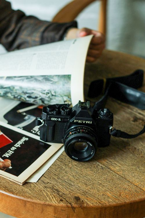 Free A classic vintage camera rests on a wooden table alongside an open book, showcasing a cozy reading and photography theme. Stock Photo