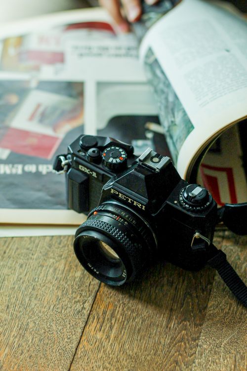 Free Vintage camera resting on a wooden table beside an open magazine, perfect for photography enthusiasts. Stock Photo
