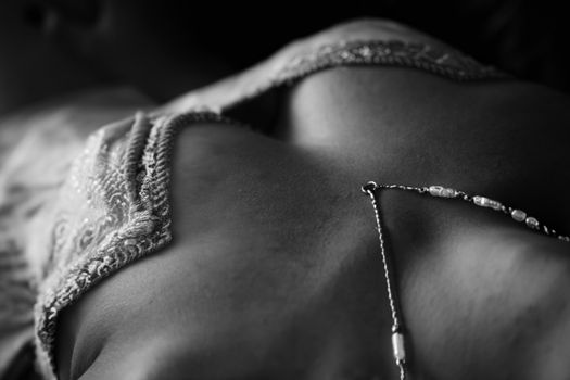 Close-up black and white image of a necklace resting on a woman's skin with intricate clothing details.