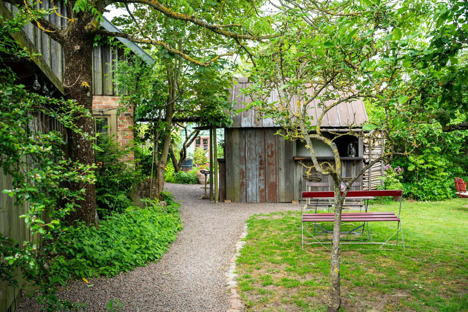 Rustic garden path with wooden sheds, lush greenery, and summer ambiance.