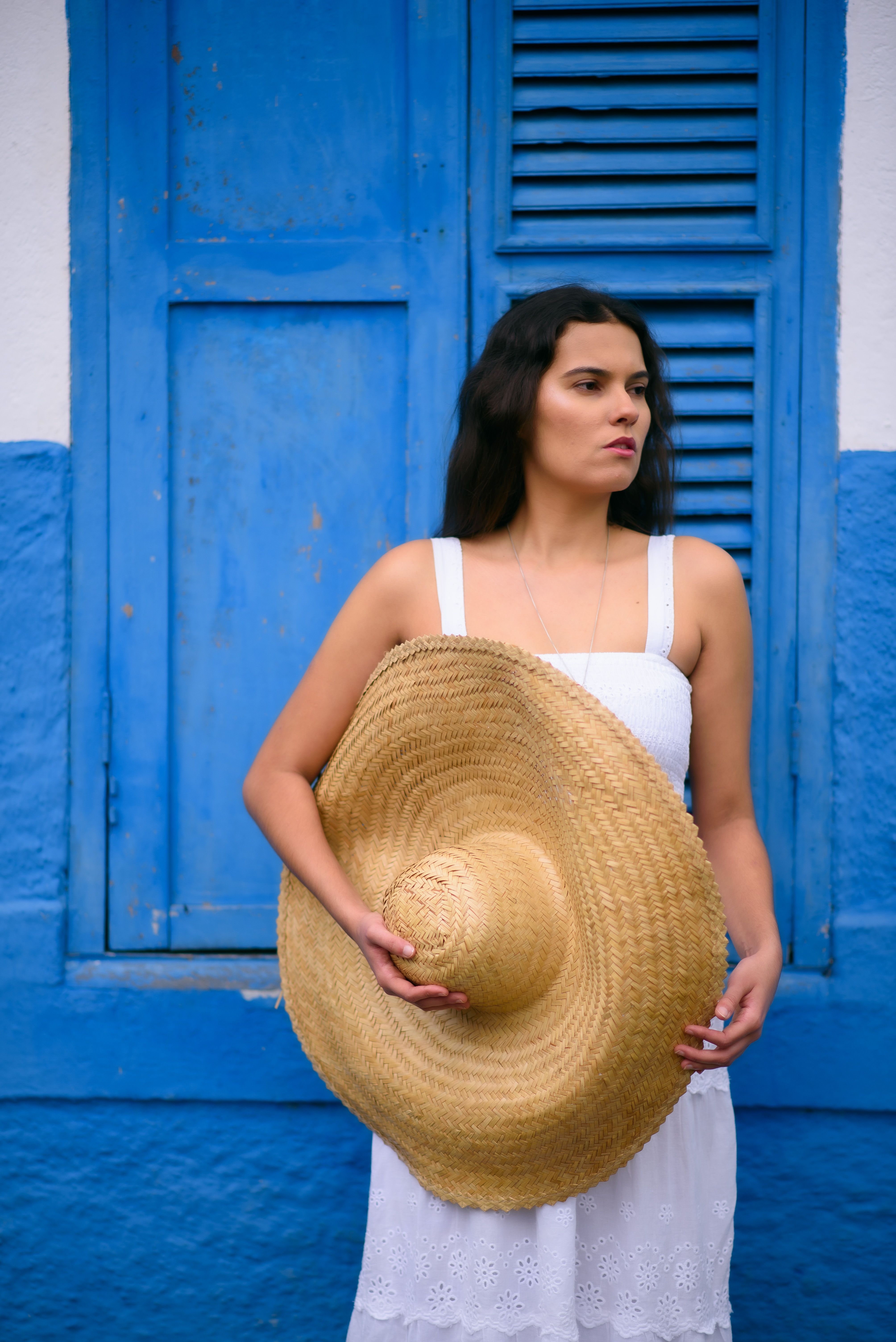 Woman in a white summer dress holding a straw hat, a vacation airport outfit idea