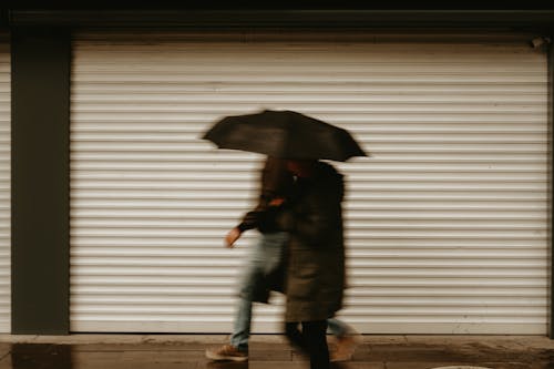 Blurred Photo of Two Men Walking with Umbrellas 