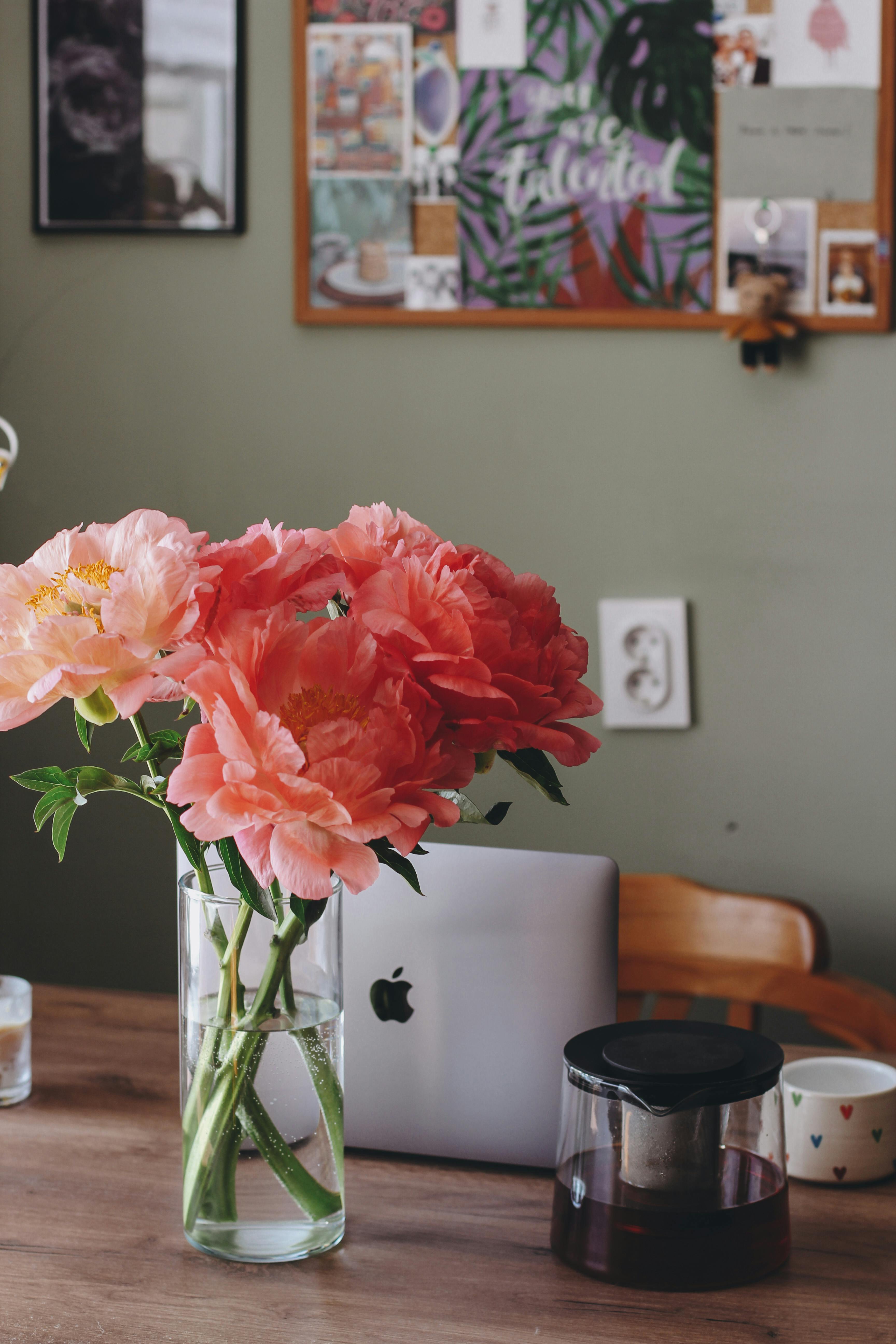 Free A cozy home workspace featuring vibrant peonies, a laptop, and decorative elements. Stock Photo