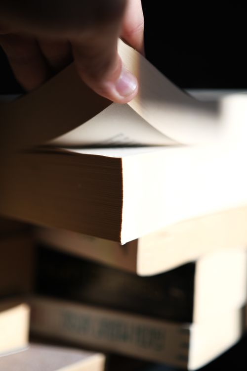 Free A hand turning pages of a book, showcasing paper texture and light contrasts. Stock Photo