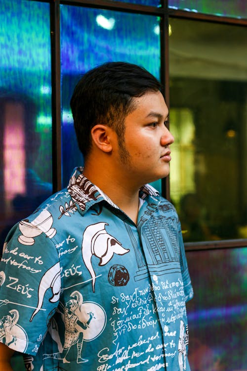 Young Man in a Blue Graphic Shirt Standing next to Windows 