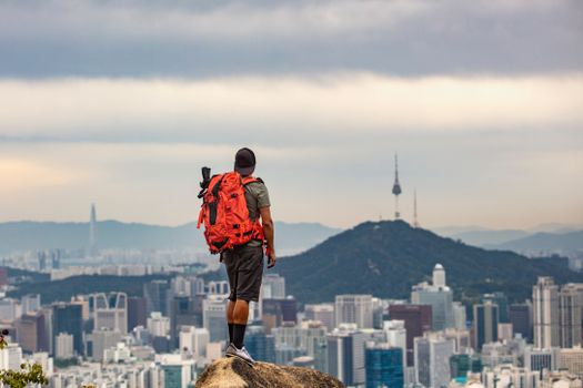 Man with backpack observing Seoul cityscape from mountain peak.