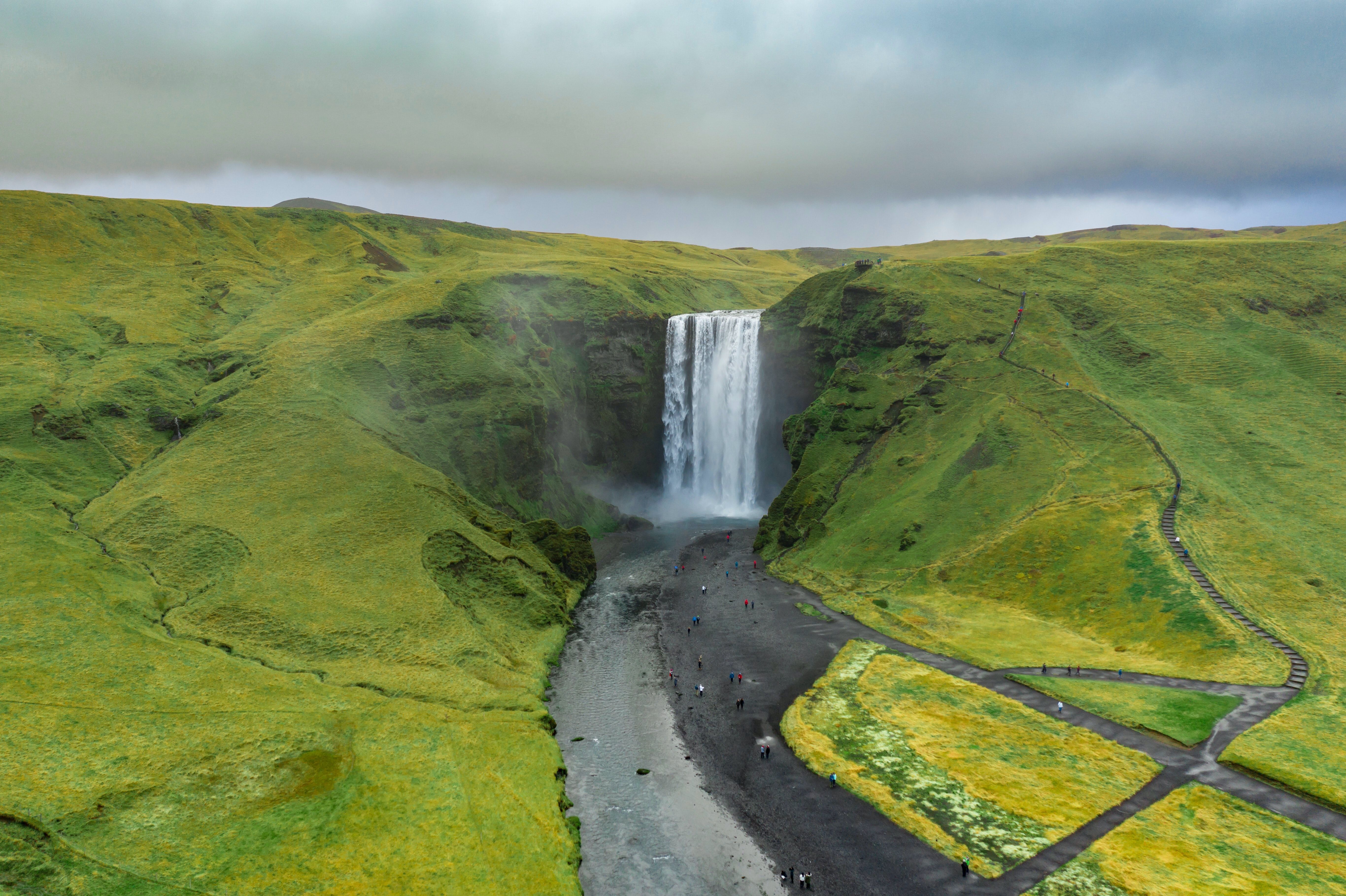 A breathtaking aerial view of Skógafoss waterfall surrounded by lush green hills and a stunning Icelandic landscape.
