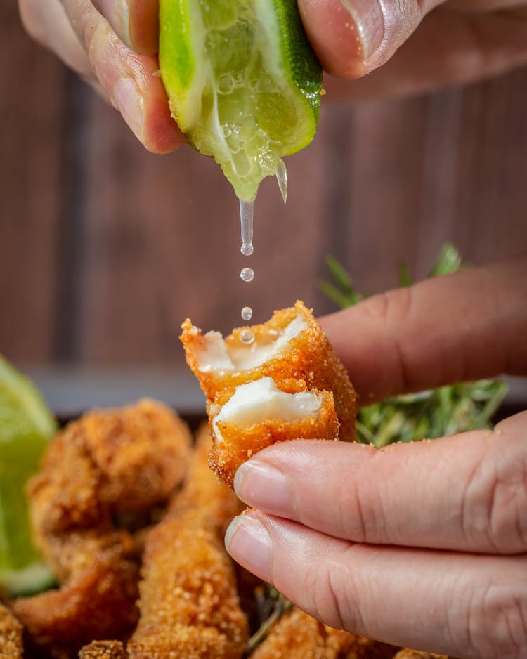 Fingers Of A Person Squeezing A Lime Juice On Fish Sticks