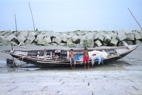 Two Boys Sitting on a Fishing Boat Lying in front of a Retaining Wall