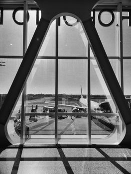 Black and white photo of airplane preparation on runway through unique airport window.