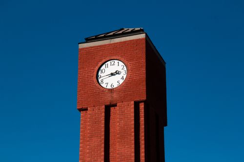 Free A red brick clock tower set against a vivid blue sky in a low-angle shot. Stock Photo