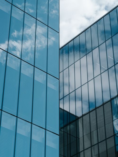 Free A low-angle shot of a contemporary glass skyscraper reflecting the sky and clouds. Stock Photo