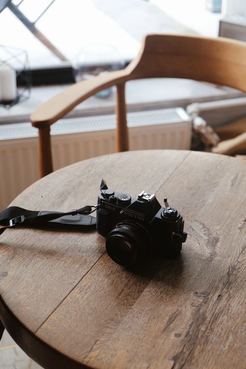 Free A retro film camera rests on a wooden table in a sunny, cozy cafe setting, evoking nostalgia. Stock Photo