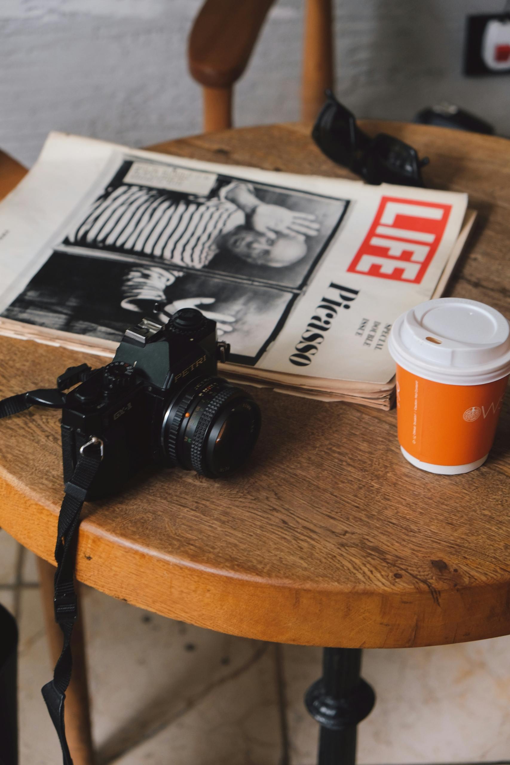A vintage camera next to a LIFE magazine featuring Picasso, on a wooden table with a coffee cup.