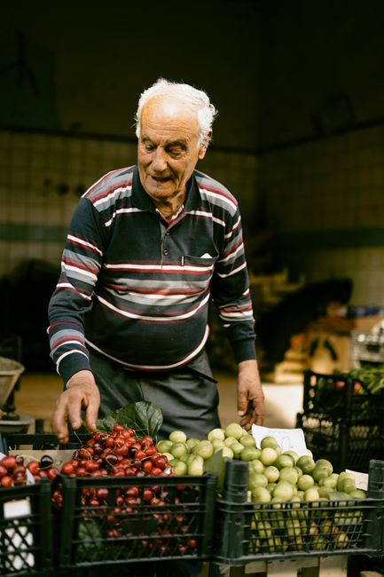 Elderly man selling fresh cherries and plums at a bustling market stall in Istanbul, Turkey.