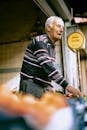 Elderly man sells fresh produce at outdoor market, vibrant scene.