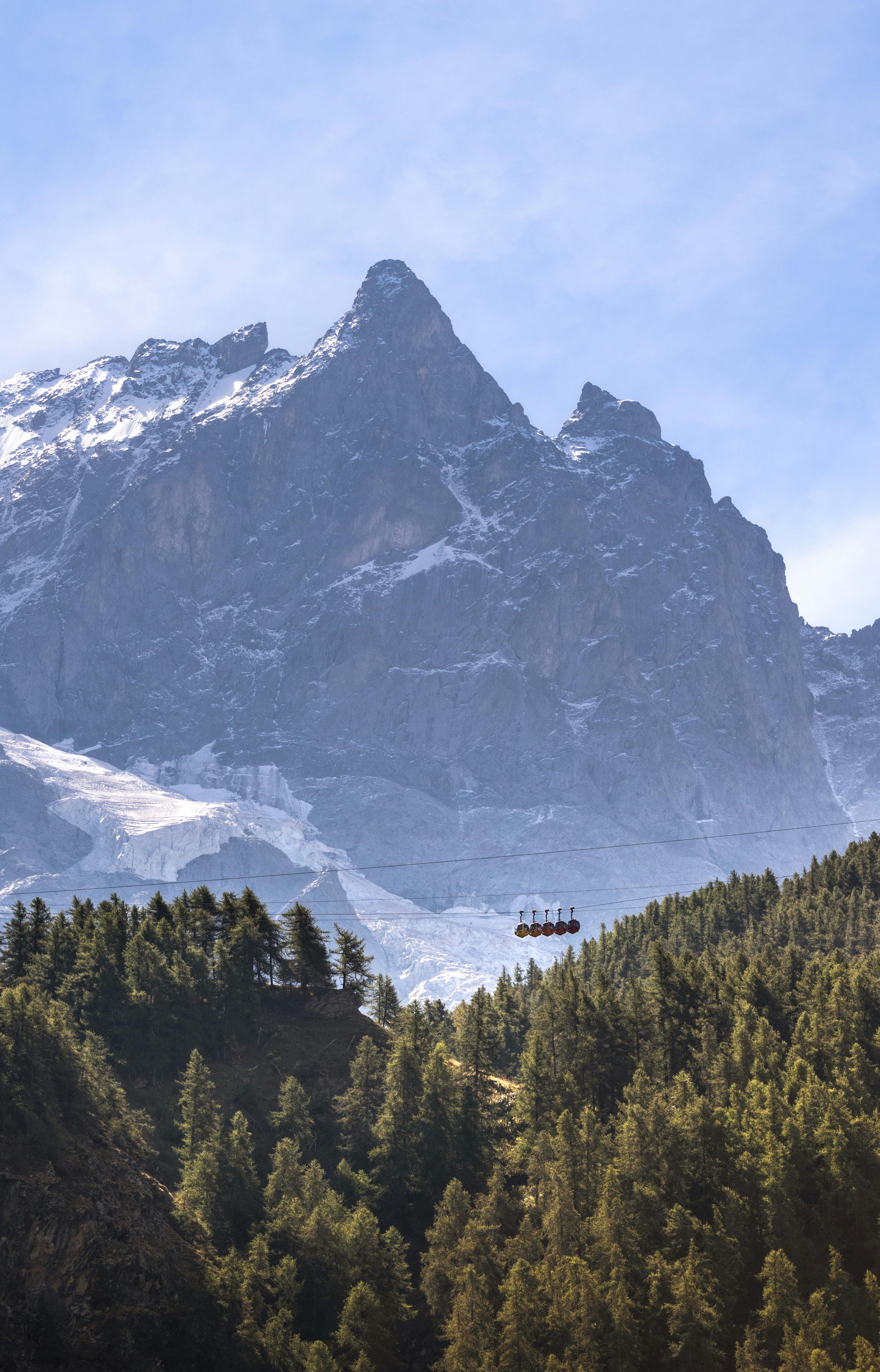 A breathtaking view of Mont Blanc with a cable car over lush forests.