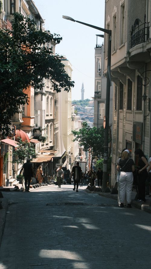 Free Narrow street in Istanbul with people walking, showcasing historic architecture and a distant minaret. Stock Photo