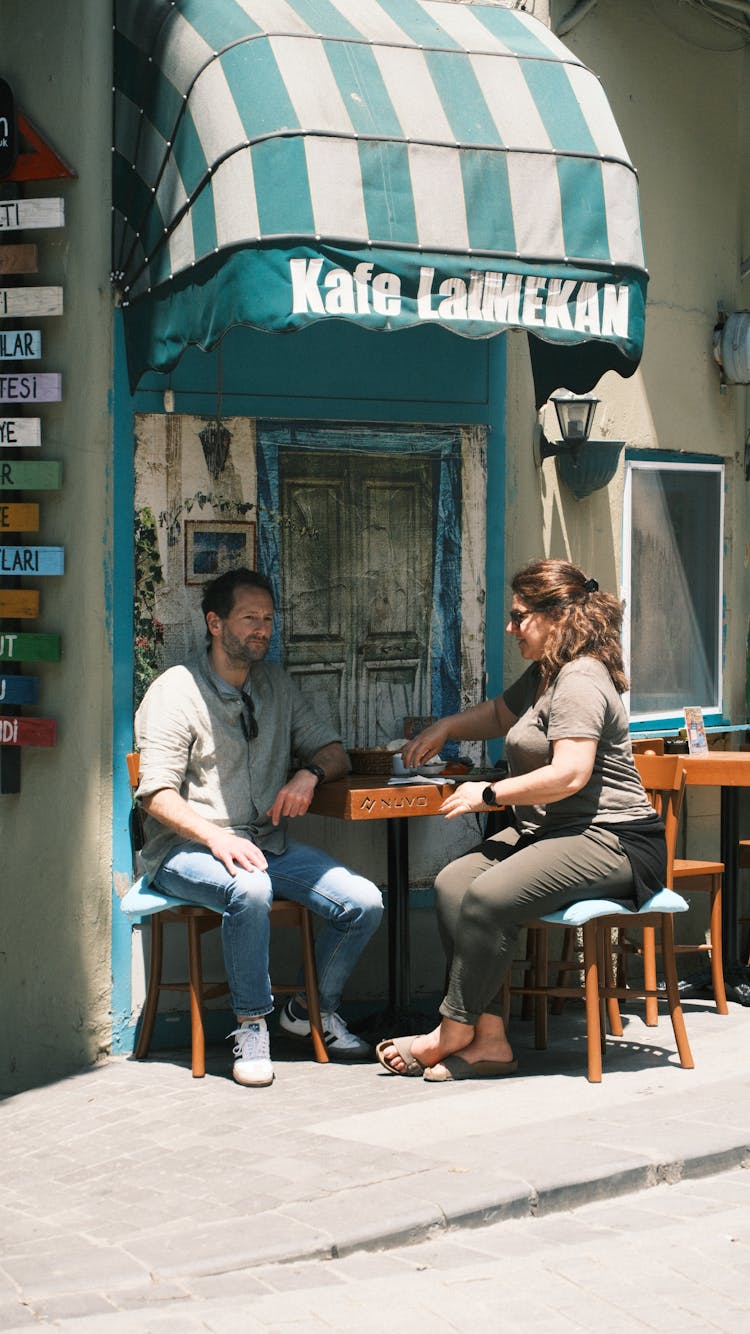 Man And Woman Sitting At The Table In A Cafe Patio 