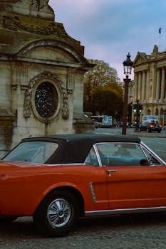Classic red car parked by historic architecture in Paris, France.