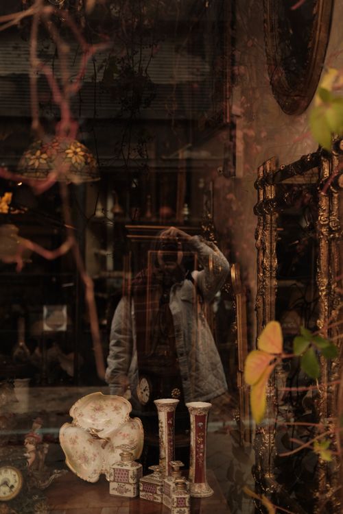 Free Photographer reflects in an antique store window showcasing vintage items. Stock Photo