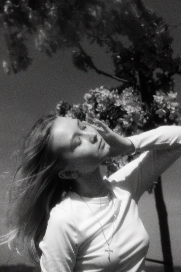 Black And White Film Photograph Of A Young Woman Standing Outside With Eyes Closed 