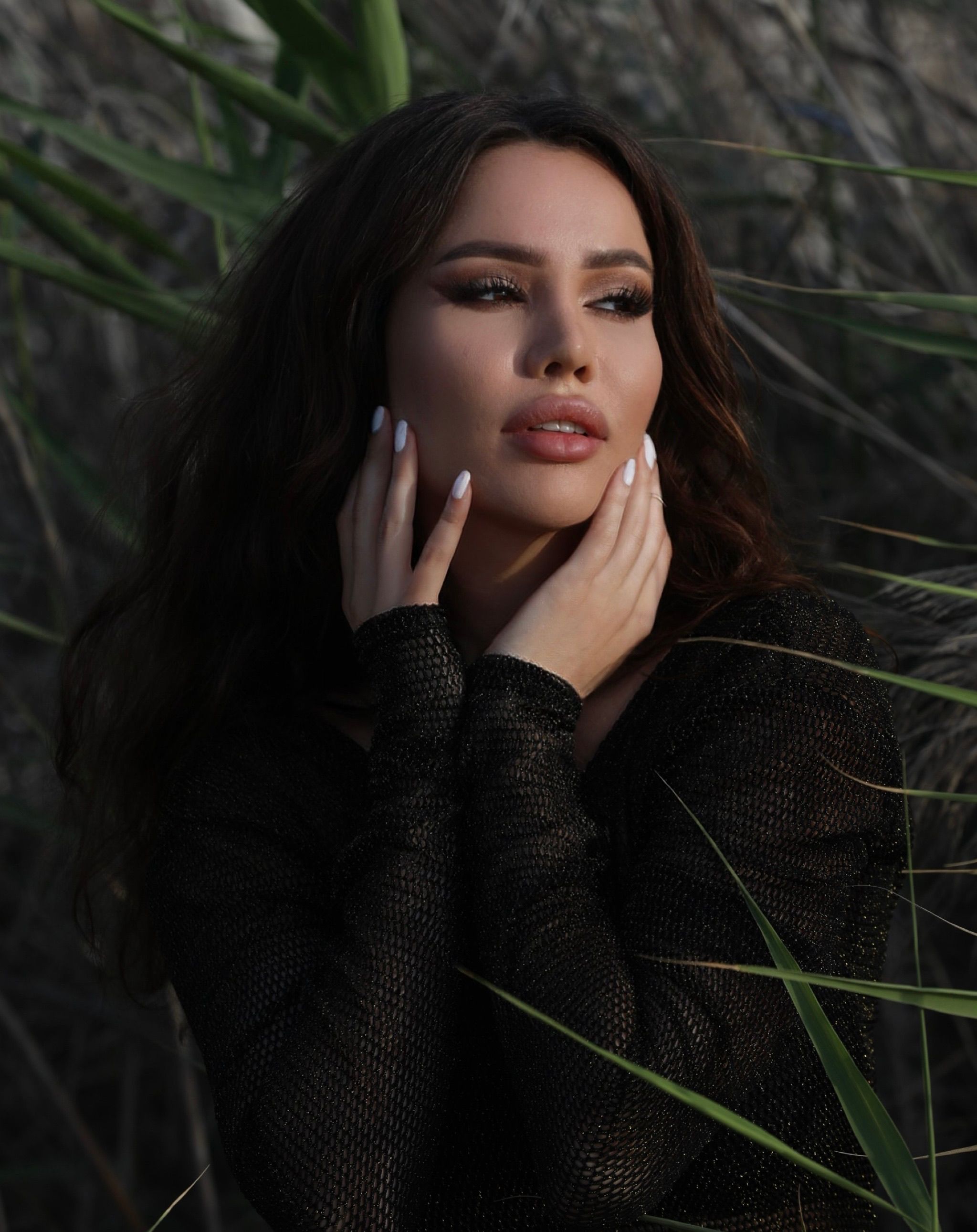 Beautiful woman in a black blouse with hands on face in a rural setting. Soft lighting and nature surrounding.