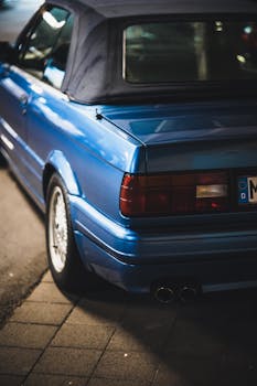 Close-up of a classic blue car parked on urban street at night, showcasing sleek design.