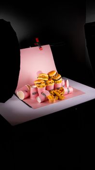 Artistic studio shot of fast food with burgers and fries on pink background.