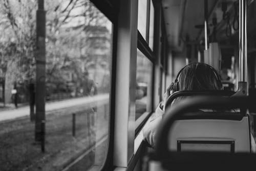 Black and White Photo of a Woman Wearing Headphones Sitting in a Bus