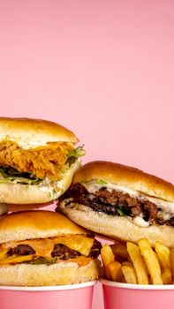 Three gourmet burgers with fries on a pink background. Perfect for fast food lovers.