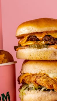 Close-up of a stacked cheeseburger and chicken sandwich with a pink background.