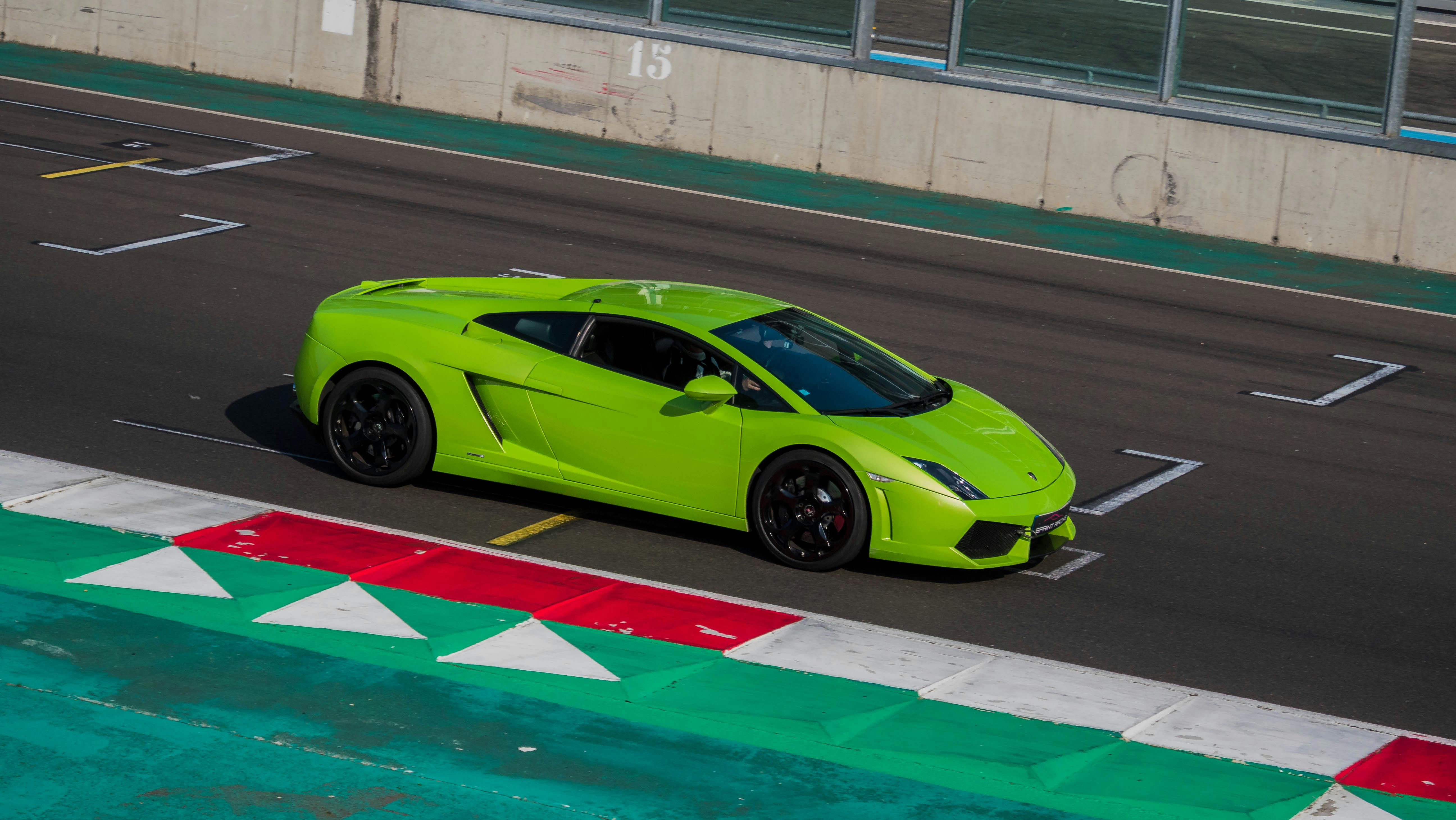 A vivid green sports car positioned at the start line on a race track during the day.