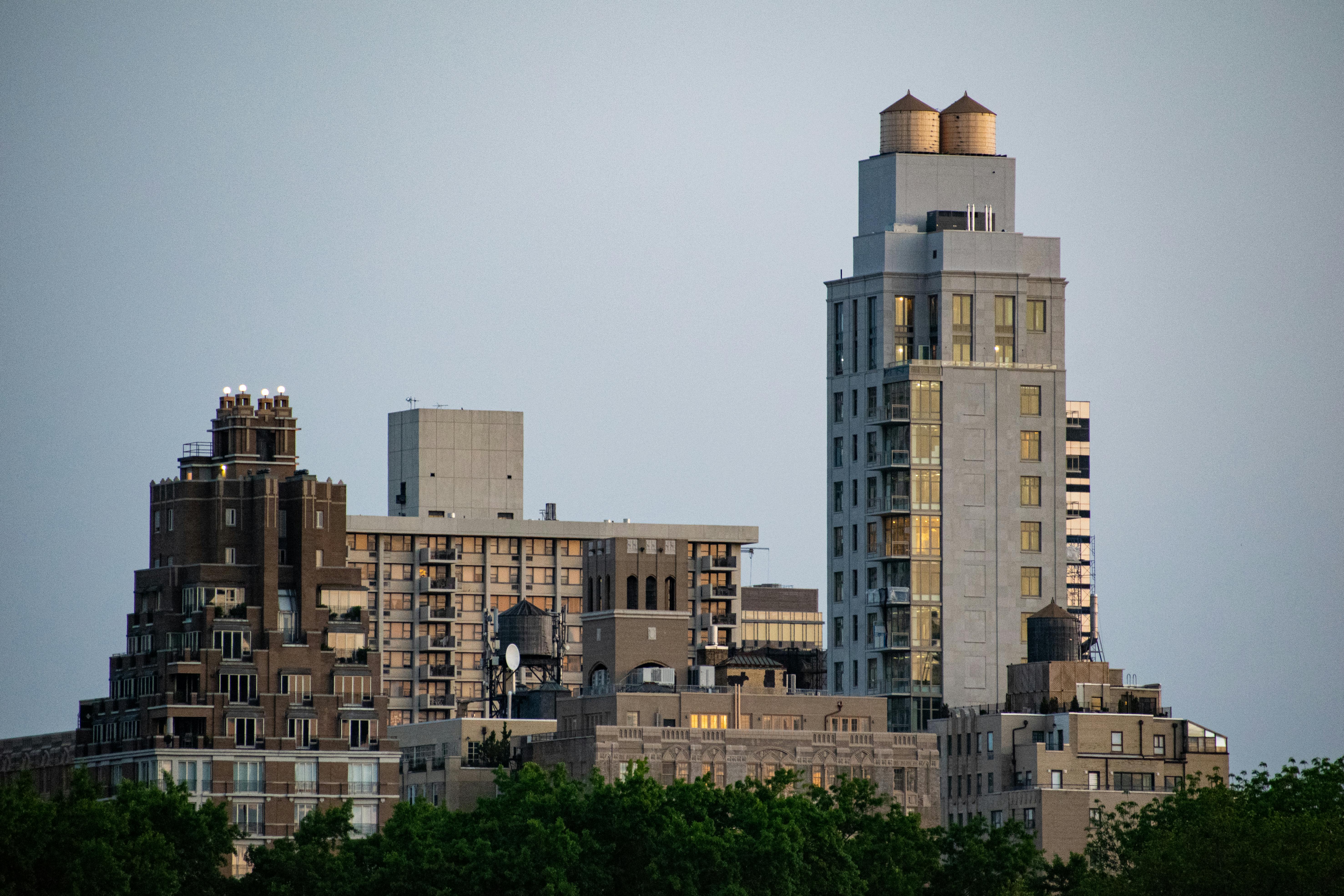 buildings of various epochs stand shoulder to shoulder bathing in the golden hues of the morning sunrise among them a modern high rise boasts two impressive water towers atop its struct