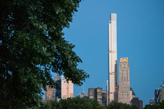 View of New York City's skyline featuring a prominent skyscraper framed by trees during twilight.