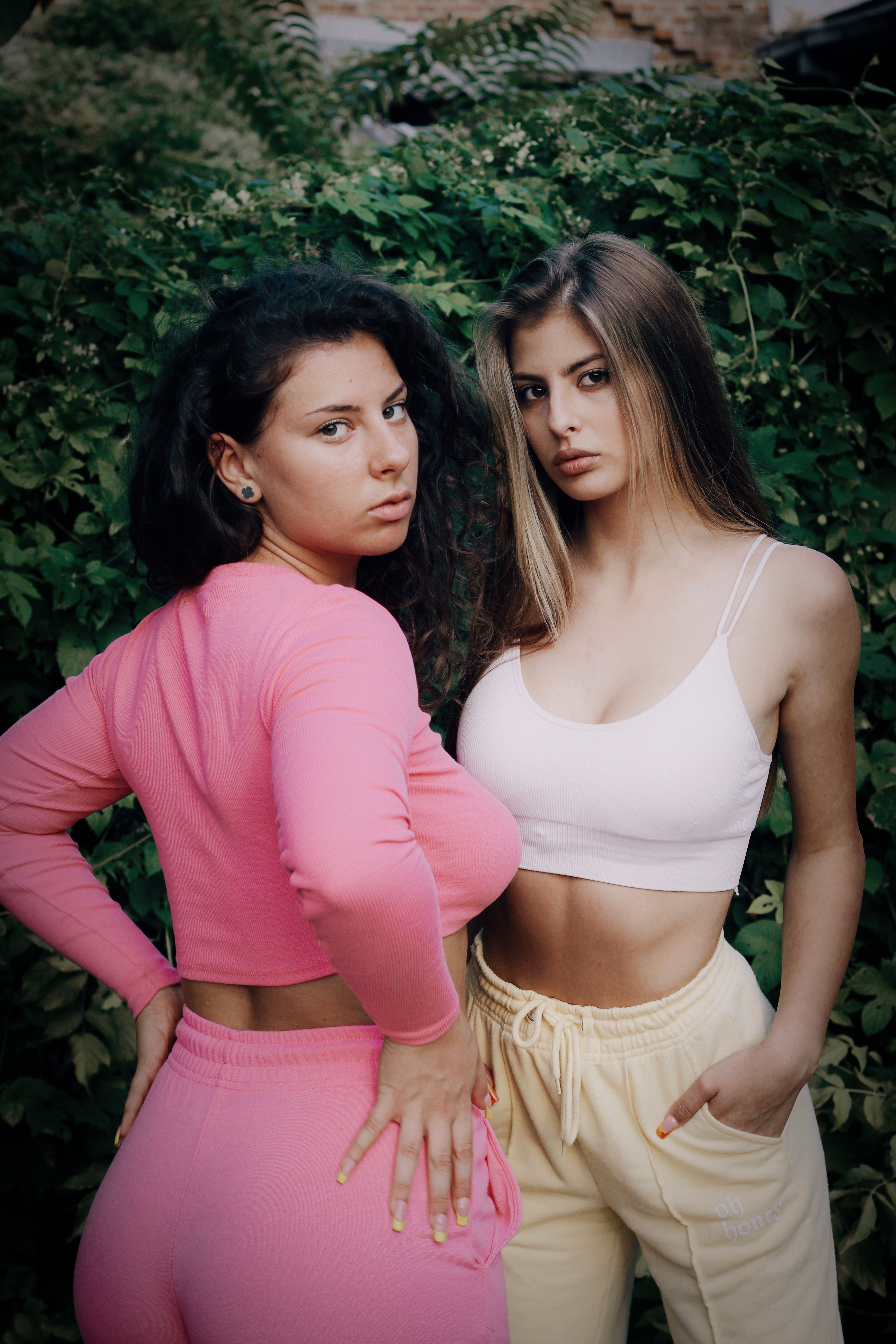 Two women in trendy outfits posing confidently in a lush outdoor environment.