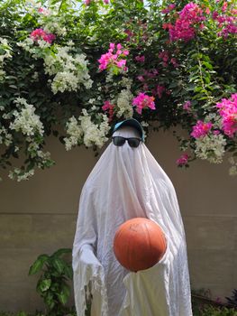 Creative shot of a ghost in sunglasses with a basketball under colorful flowers.