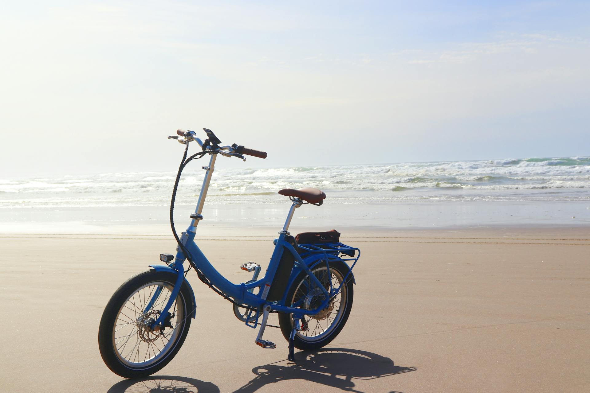 Blue electric bike on sandy Cannon Beach, Oregon, with waves in the background.