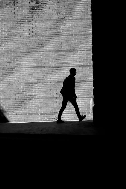 Silhouette of a Man Walking in City on the Background of a Brick Wall 