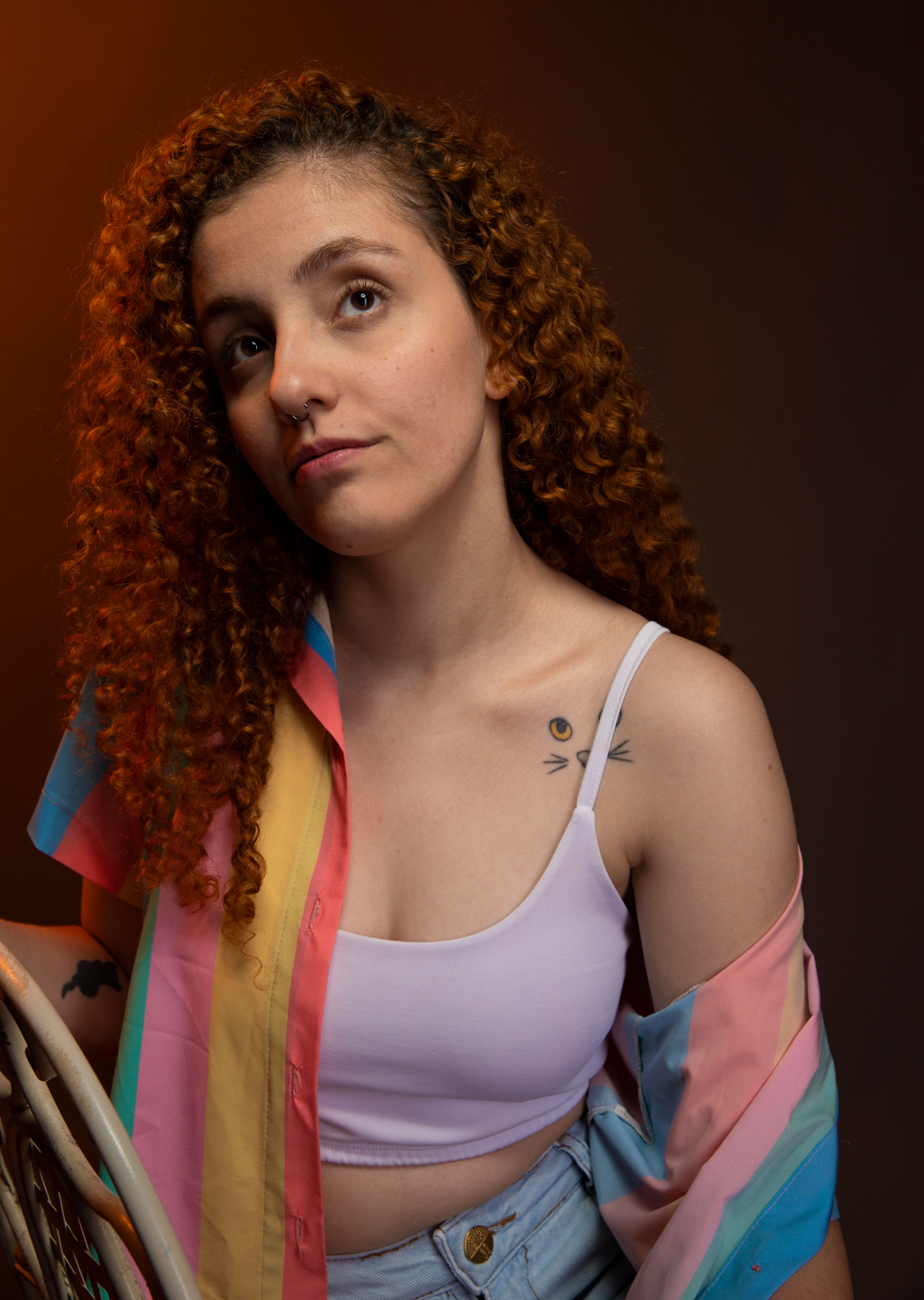 Stylish portrait of a young redhead woman with curly hair and tattoos in a studio setting.