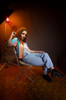 A fashionable young woman with curly hair poses in a studio setting, showcasing vibrant and casual style.
