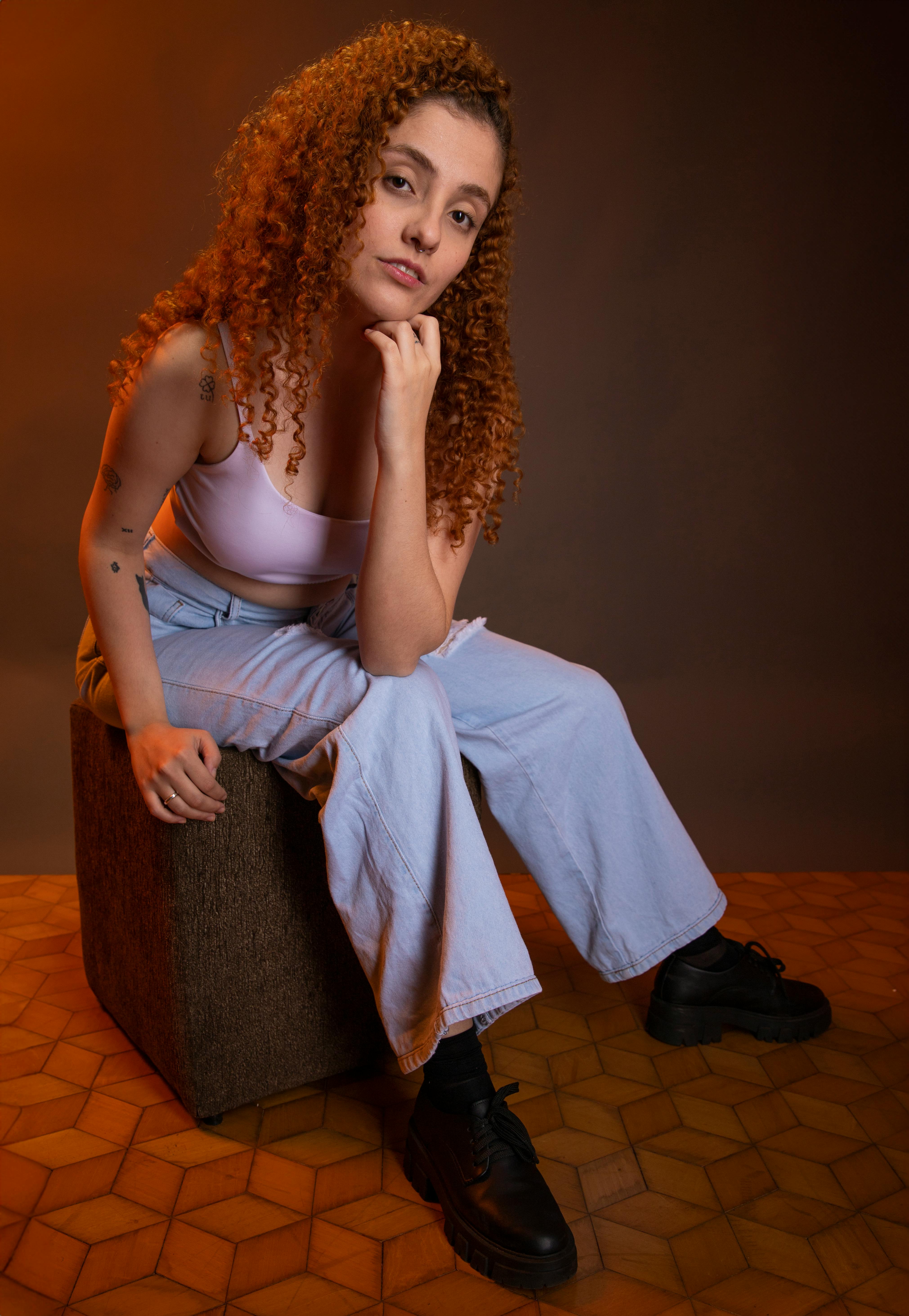 Young woman with curly hair posing indoors on a cube. Fashion portrait with warm tones.