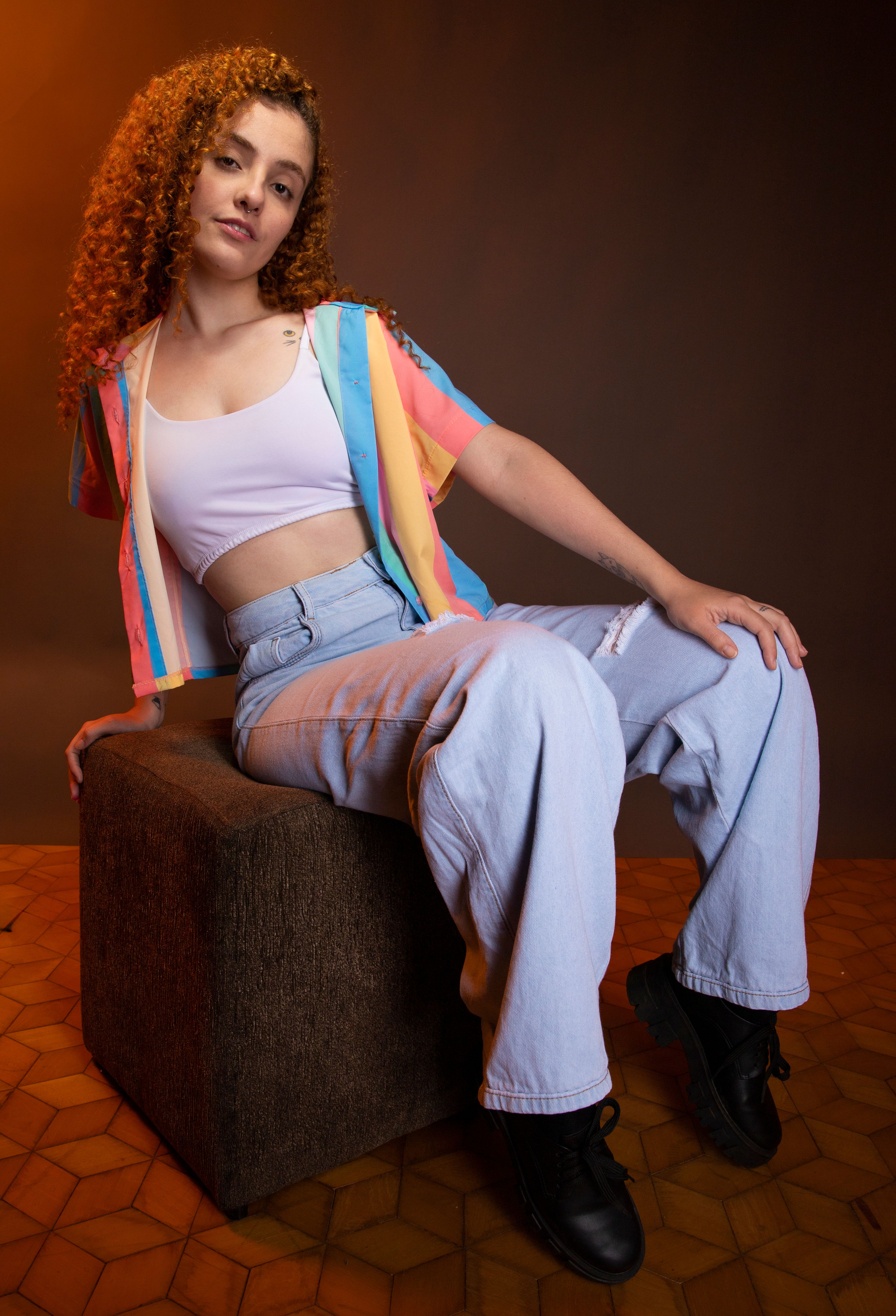 Chic studio portrait of a young woman with curly hair in a colorful crop top and jeans, exuding fashion-forward style.