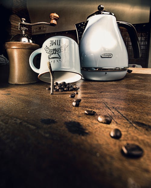 Close-up of Coffee Beans Forming a Trail Toward a Mug Standing next to a Grinder and Kettle 