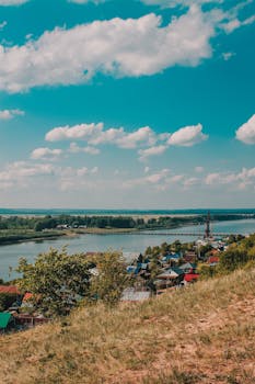 Charming village scene overlooking a tranquil river under a vibrant summer sky.